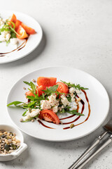 Healhy salad with arugula, cherry tomatoes and feta cheese with cutlery on white background. Green diet vegetarian salad concept with copy space