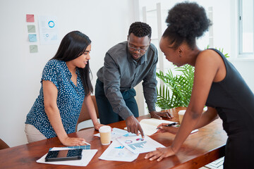 Three colleagues stand around conference table meeting about financial reports strategy