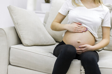 Crop photo of pregnant woman sitting on white sofa.