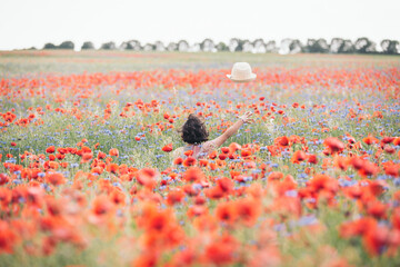 Latina girl in the middle of a poppy field with her hat in the air
