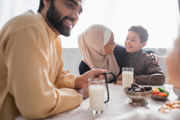 Positive african american mother in hijab hugging son near family and suhur breakfast at home.