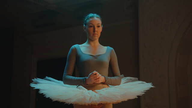 Cinematic shot of graceful ballerina in ballet dress standing in theater lobby after choreography rehearsal, looking at camera. Beautiful female ballet dancer before performance. Classical ballet art.