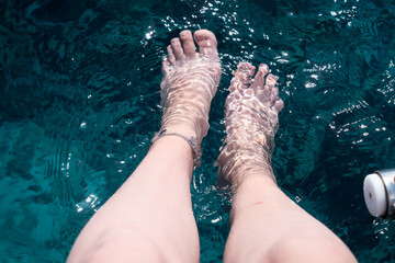 Pair of female legs with manicure on a blue sea background