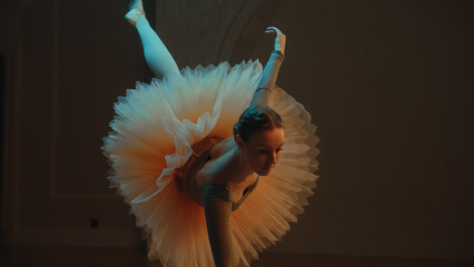 Cinematic shot of graceful ballerina in ballet tutu performing in dim opera lobby and practicing gymnastic movement. Female ballet dancer on choreography rehearsal in theater. Classical ballet art.