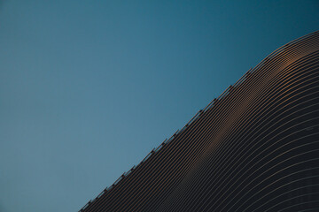Black building made of parallel lines kissed by sunset before a blue sky, shopping centre, mall,...