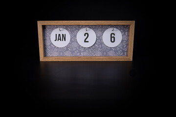 A wooden calendar block showing the date January 26th on a dark black background, save the date or date of event concept