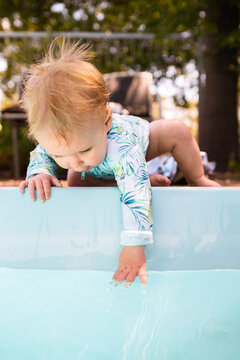 Young baby leaning over edge of inground swimming pool splashing in water &ndash; dangerous situation