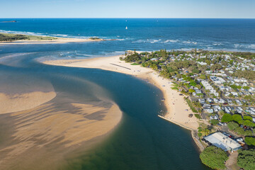 Aerial view of waterfront property alongside a blue coastal river mouth with tidal sandbars