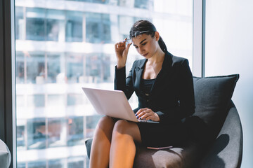Fototapeta premium Serious businesswoman working on laptop near window