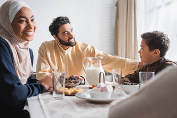 Muslim father looking at son near family during suhur in morning at home.