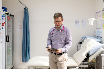 Male doctor holding a tablet with a stethoscope around his neck standing in the clinic