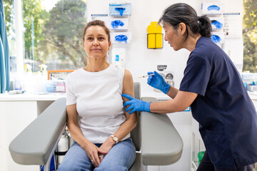 Female patient getting an injection on the arm by a female healthcare practitioner in a clinic