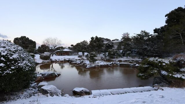 Peaceful view of pond in snowy park and Akashi Castle tower at dawn
