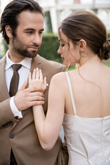 bearded man in suit with tie looking at pretty bride outdoors.