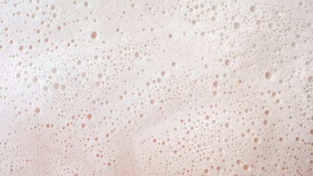 Macro shot of water wave flows creating foam on beige background | Background shot for skin hydration cosmetics commercial