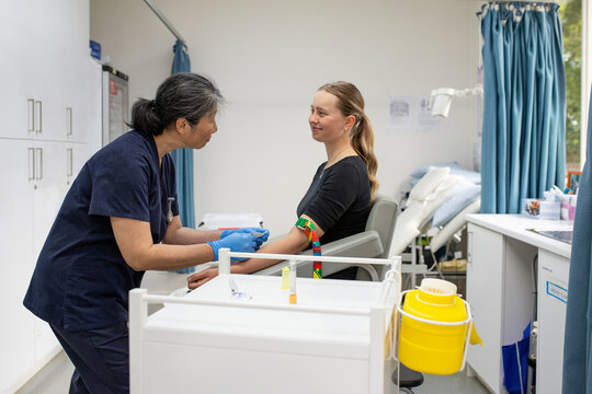 Female Health Care Working Talking To A Female Patient While Putting Tourniquet On Her Arm