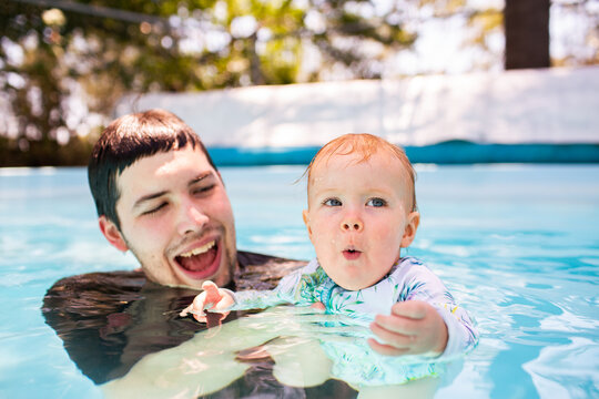 baby with excited expression in swimming pool water with parent
