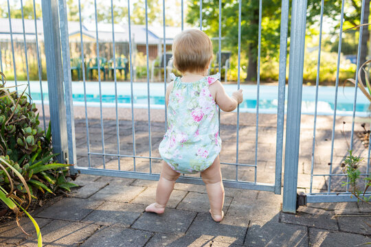 Young child standing at self closing pool gate safe behind fence