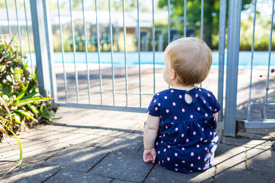 Young baby sitting at backyard pool gate fence in summer