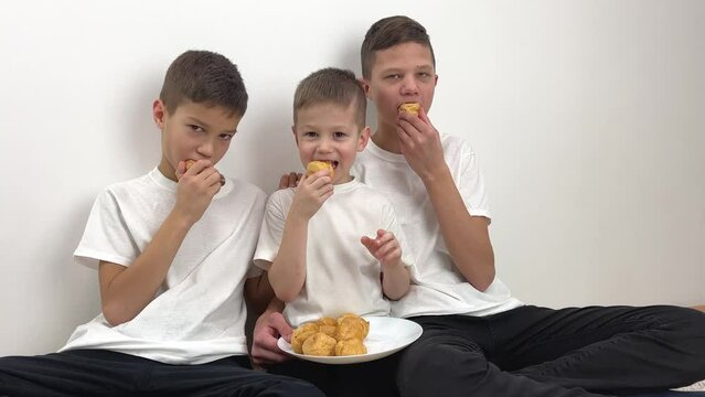 three boys bratya friends of different ages teenagers eat custards with cream on white background home comfort Friendship share white top black bottom communication tasty sweets