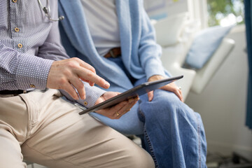 Close up shot of a tablet with the a doctor holding it while talking to a woman in the clinic