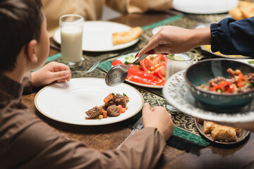 Muslim mother serving food on plate near son and ramadan dinner at home.