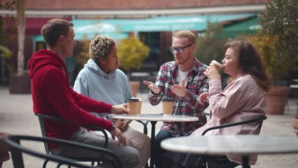 Happy multiracial young people friends talking laughing at group meeting in outdoors cafe. Realtime