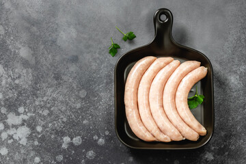 Raw chicken sausages on dark ceramic dish, cast iron skillet, dark background. Top view, copy space.