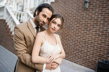 young groom in beige suit hugging gorgeous bride in white wedding dress.