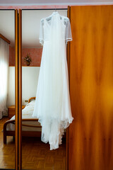 Beautiful wedding dress hanging on a wooden wardrobe before preparation