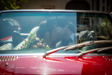 Happy newlyweds on their wedding day leave for their honeymoon in a red sports car