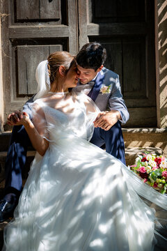 Romantic image of a bride and groom holding hands sitting in front of a wooden door of an ancient Italian villa.