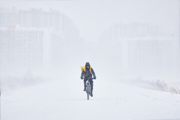 a man on a bicycle in a snowstorm in the city the concept of a fast delivery service in any weather on time