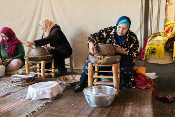 Three women working on production of traditional grind of argan nuts to make oil in a cooperative