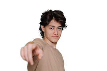 Confident young teen in beige t-shirt points at camera by index finger standing against transparent background with empty space. Handsome schoolboy with wavy hair smiles looks at camera. Choice mockup