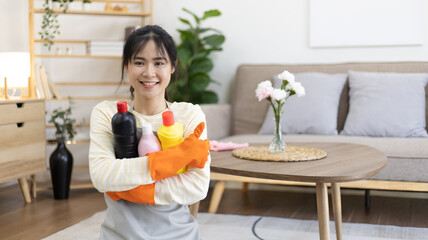 Asian housewife wearing apron and gloves holding toilet cleaner preparing to clean the bathroom,...