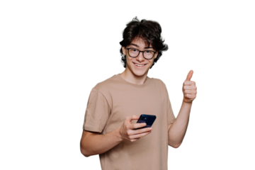 Handsome teenager in glasses and beige t-shirt holds phone shows thumb up gesture looks at camera toothy smiles standing against transparent background. Smart Italian boy approve choice. Mockup .