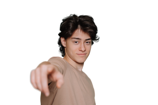 Confident young teen in beige t-shirt points at camera by index finger standing against transparent background with empty space. Handsome schoolboy with wavy hair smiles looks at camera. Choice mockup
