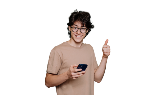 Handsome teenager in glasses and beige t-shirt holds phone shows thumb up gesture looks at camera toothy smiles standing against transparent background. Smart Italian boy approve choice. Mockup .