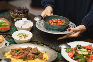 Cropped view of muslim woman holding delicious meal near table during ramadan dinner.
