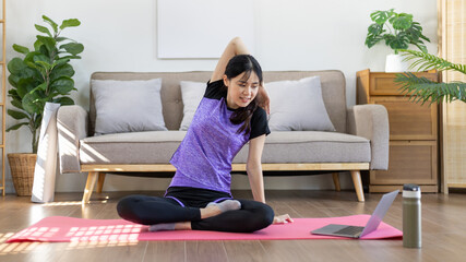 Obraz premium Beautiful healthy woman practicing yoga, Stretch or warm up before exercising, Calming the mind and meditating in her living room, Dumbbells and a protein shake or bottle of water, Healthy exercise.