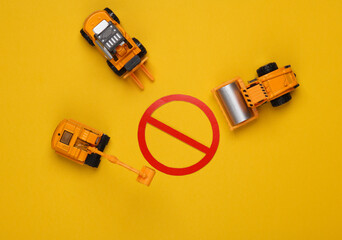 Toy heavy machinery with a prohibition sign on yellow background. Top view