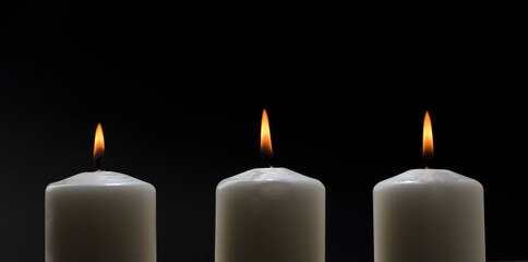 three burning candles on white table with black background, space for text