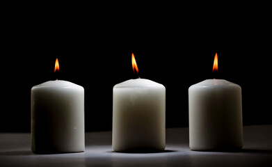 Obraz na płótnie Canvas three burning candles on white table with black background, space for text