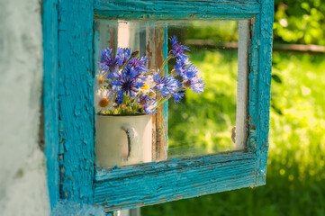 A bouquet of wildflowers and cornflowers on an old rustic window to the garden.
