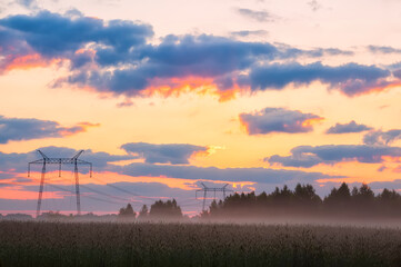 Early morning in a field with fog. Huge poles with power lines in a foggy field at dawn.