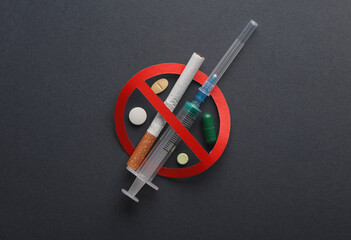 Let's stop drug addiction. Syringe and cigarette, pills with prohibition sign on dark background