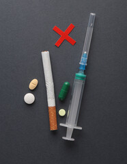 Let's stop drug addiction. Pill syringe and cigarette with prohibition cross on dark background