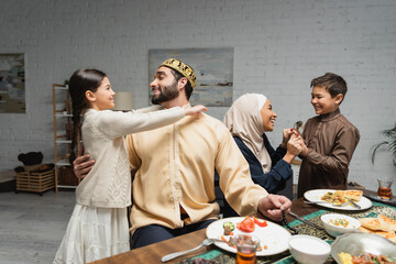 Cheerful middle eastern family hugging and talking during ramadan dinner at home.