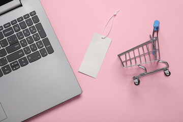 Price tags with laptop and shopping trolley on pink background. Online shopping. Top view